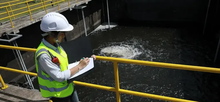 Técnica de capacete e colete refletivo faz anotações junto a um tanque de tratamento de água