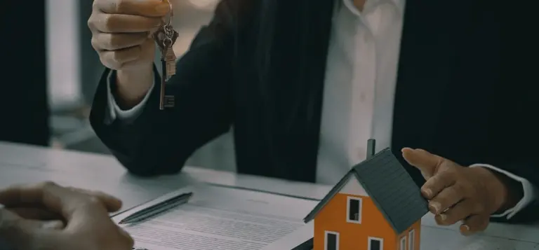 Mão entrega um molho de chaves sobre a maquete de uma casa