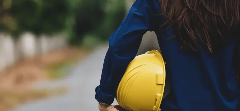 Mulher de costas segurando um capacete de obra amarelo