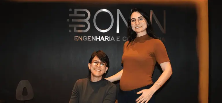 Duas mulheres posam sorrindo diante do letreiro da Bonin Engenharia