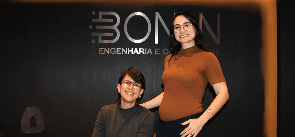 Duas mulheres posam sorrindo diante do letreiro da Bonin Engenharia